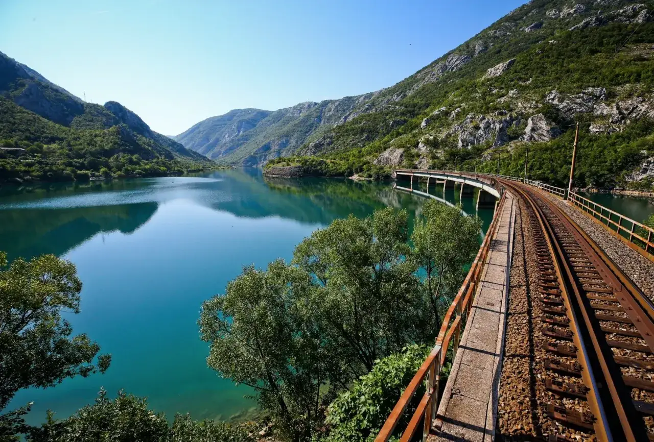 Eisenbahnbr&uuml;cke &uuml;ber einen t&uuml;rkisfarbenen See in einer Berglandschaft, die den Sarajevo-Mostar-Zug-Weg s&auml;umt.