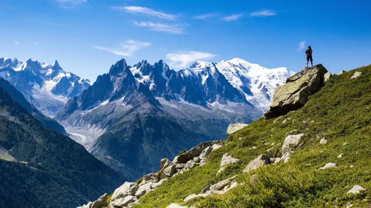 Ein Wanderer steht auf einem Felsen und blickt auf die majest&auml;tische Bergkulisse des Mont Blanc. Die schneebedeckten Gipfel und Gletscher sind beeindruckend.