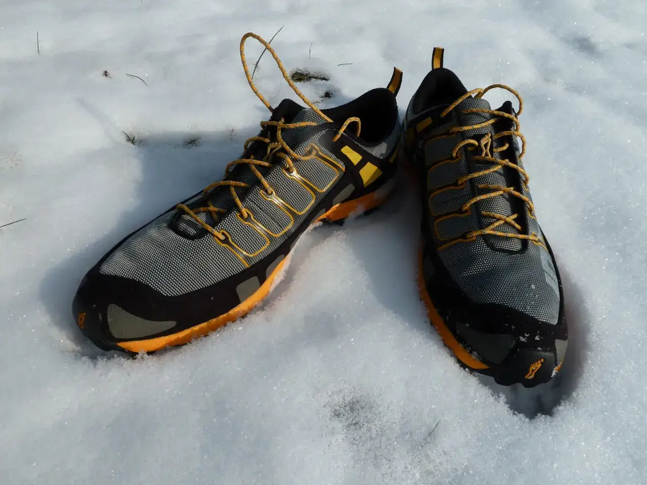 Graue und orangefarbene trailrunningschuhe zum wandern liegen im Schnee.