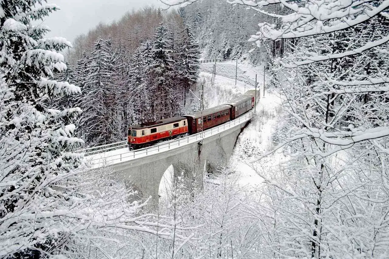 Roter Zug der slowakischen Bahn f&auml;hrt &uuml;ber eine verschneite Br&uuml;cke im Winterwald.