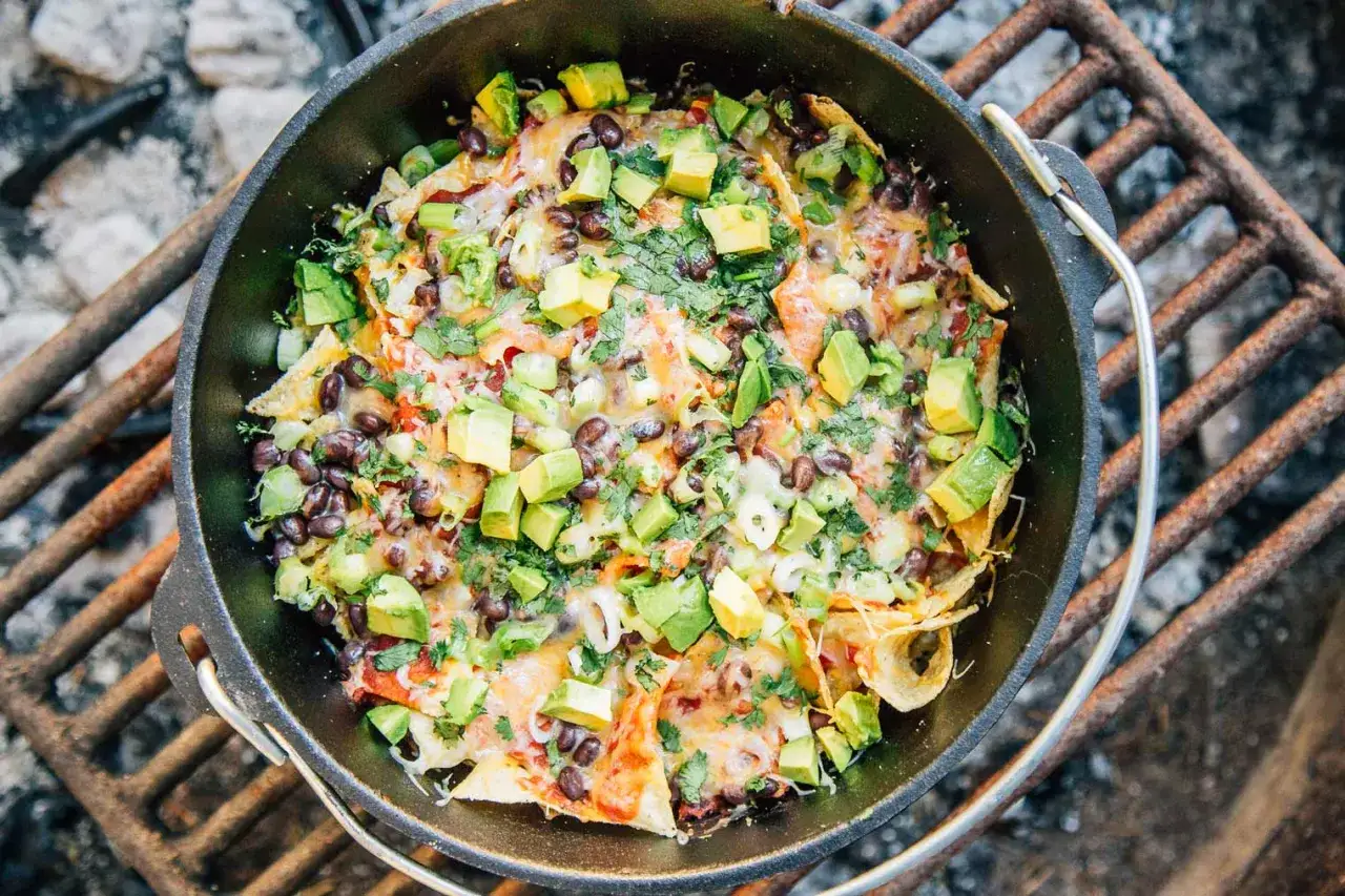 Schwarze Bohnen-Nachos mit Avocado und Koriander, zubereitet in einem Gusseisentopf über dem Feuer – ein perfektes Beispiel für einfache Outdoor-Gerichte.