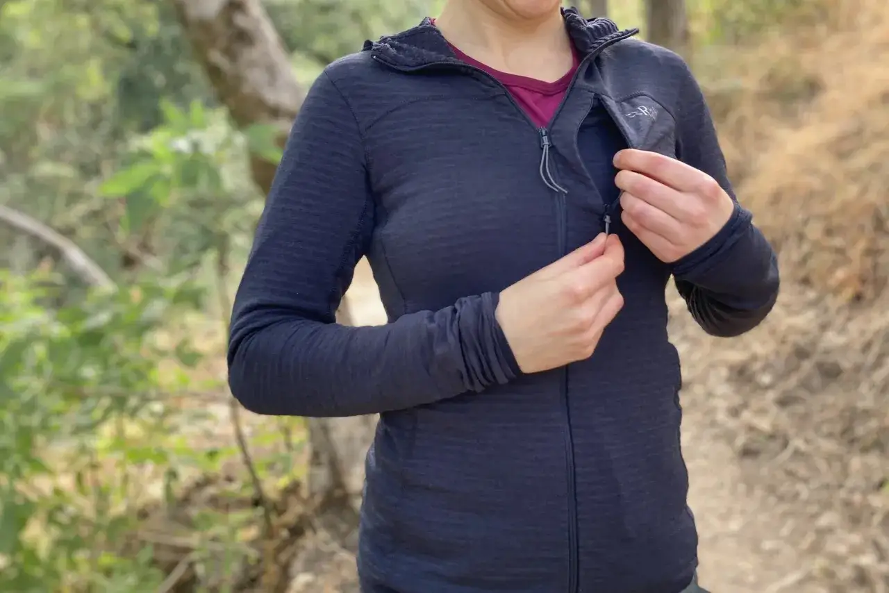 Frau schlie&szlig;t Rei&szlig;verschluss einer dunkelblauen Fleecejacke. Das Material ist weich und warm, ideal f&uuml;r Outdoor-Aktivit&auml;ten.