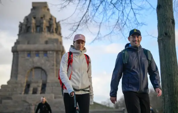 Ein Paar genießt eine Wanderung, passend mit wetterfester Wanderkleidung und Rucksäcken ausgestattet, vor einem imposanten Denkmal.