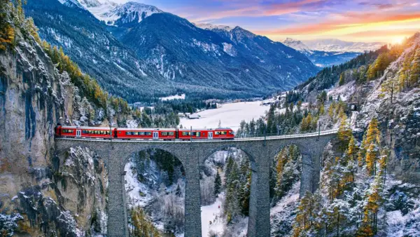 Roter Zug überquert eine Steinbrücke in verschneiter Schweizer Alpenlandschaft. Ein perfektes reiseziel schweiz.