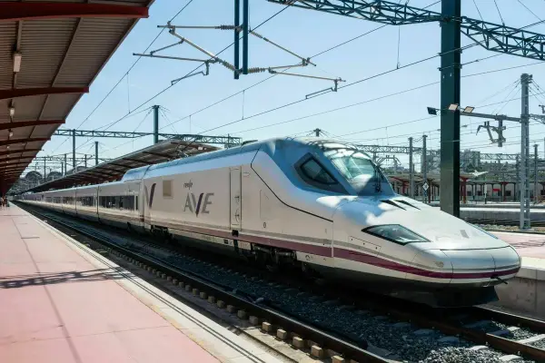 Moderner, weißer Renfe ave zug mit lila Akzenten steht auf Gleisen unter einem Bahnhofsdach.