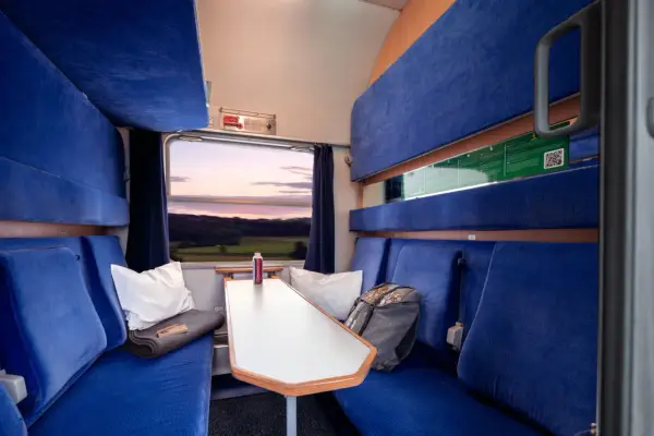 Gemütliche Kabine im Holland Zug mit blauen Sitzen, einem Tisch und Blick auf die Landschaft bei Sonnenuntergang.