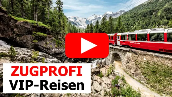 Ein roter Panoramazug fährt über eine Steinbrücke durch eine Berglandschaft mit Wäldern und schneebedeckten Gipfeln.